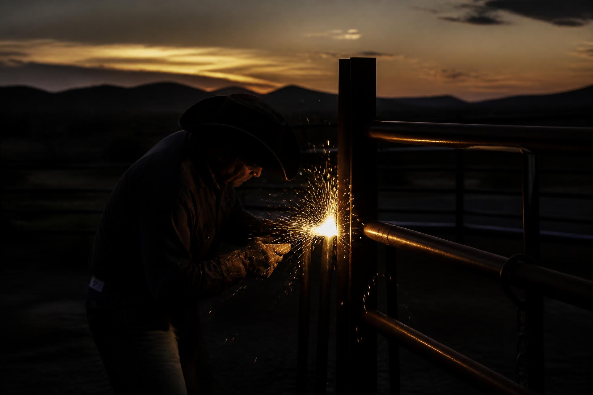 Ranch hand welding a steel gate at golden hour